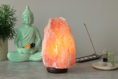 Photo of Himalayan salt lamp, buddha figure, incense and crystals on stone table near grey wall
