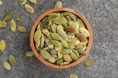 Wooden bowl with peeled pumpkin seeds on grey table, flat lay