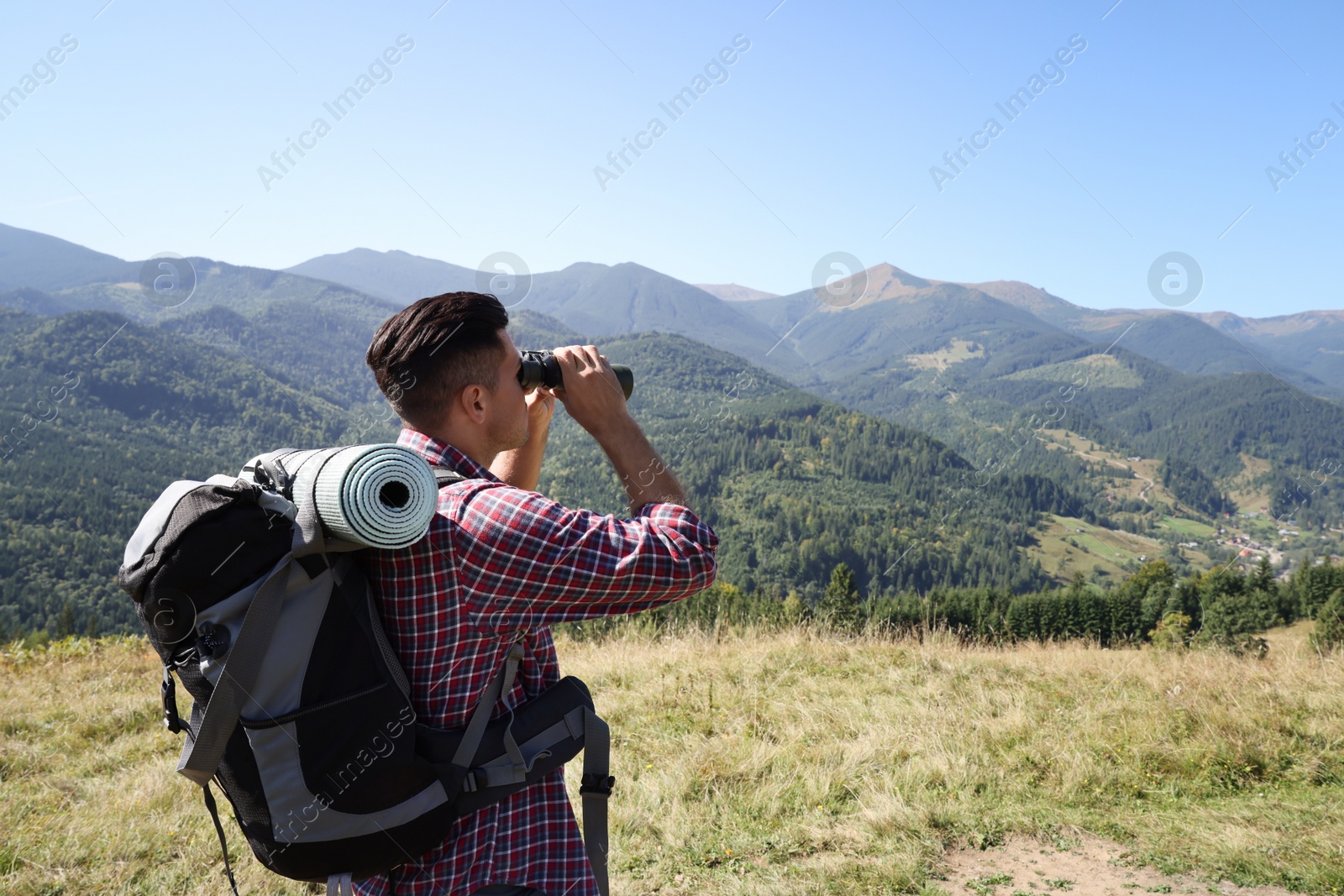 Photo of Tourist with backpack and sleeping pad looking through binoculars in mountains