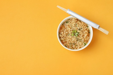Photo of Cup of cooked instant noodles with chopsticks on color background, top view. Space for text