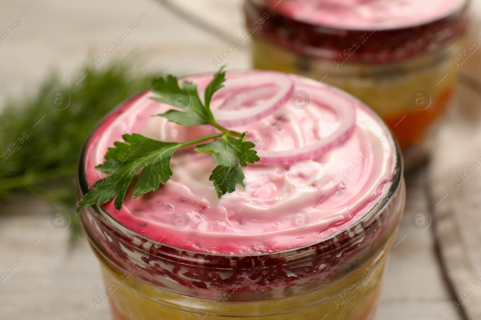 Photo of Glass jars of herring under fur coat on wooden table, closeup. Traditional Russian salad