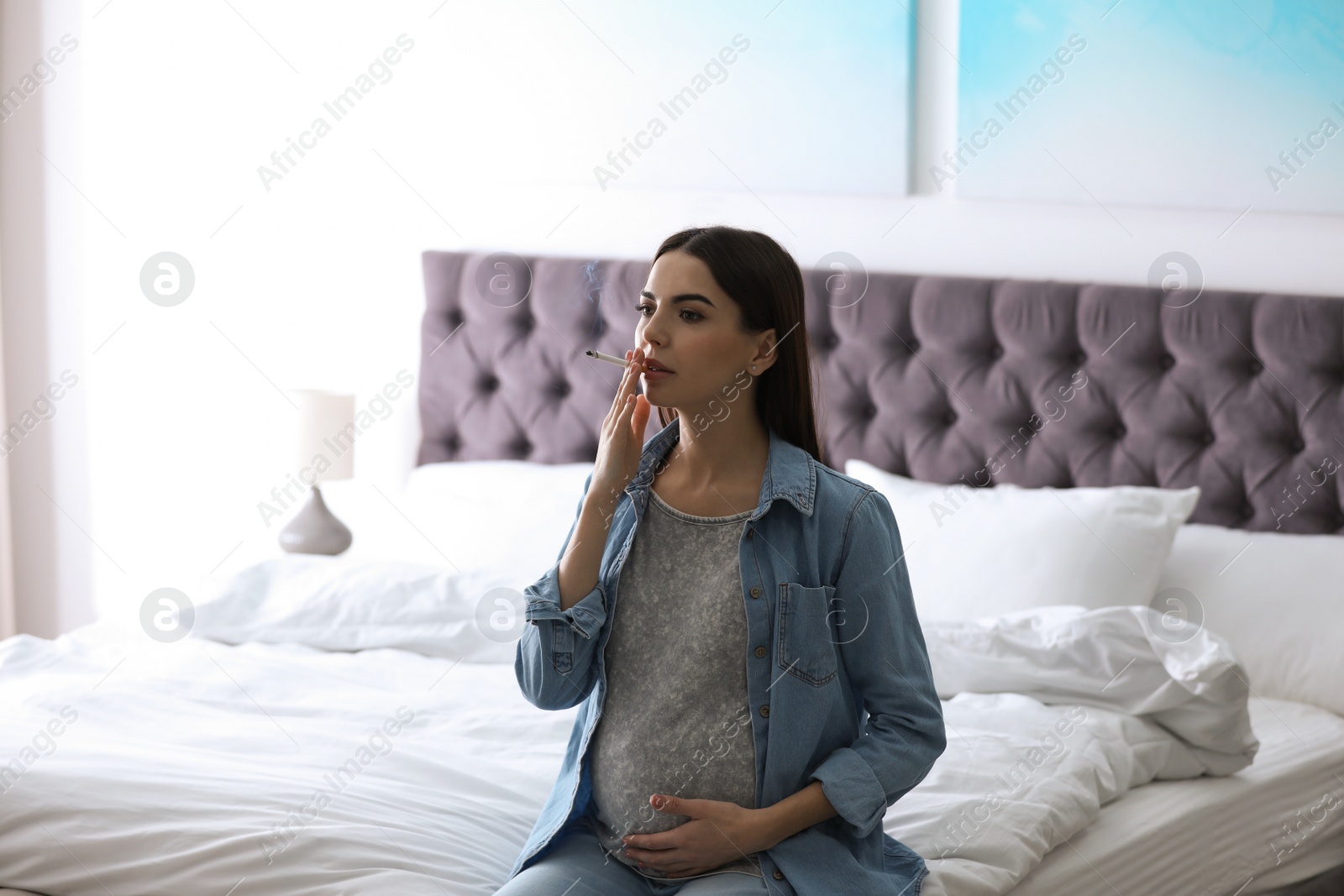 Photo of Young pregnant woman smoking cigarette at home