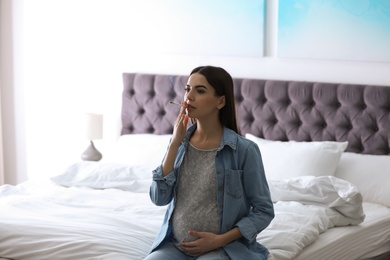 Photo of Young pregnant woman smoking cigarette at home