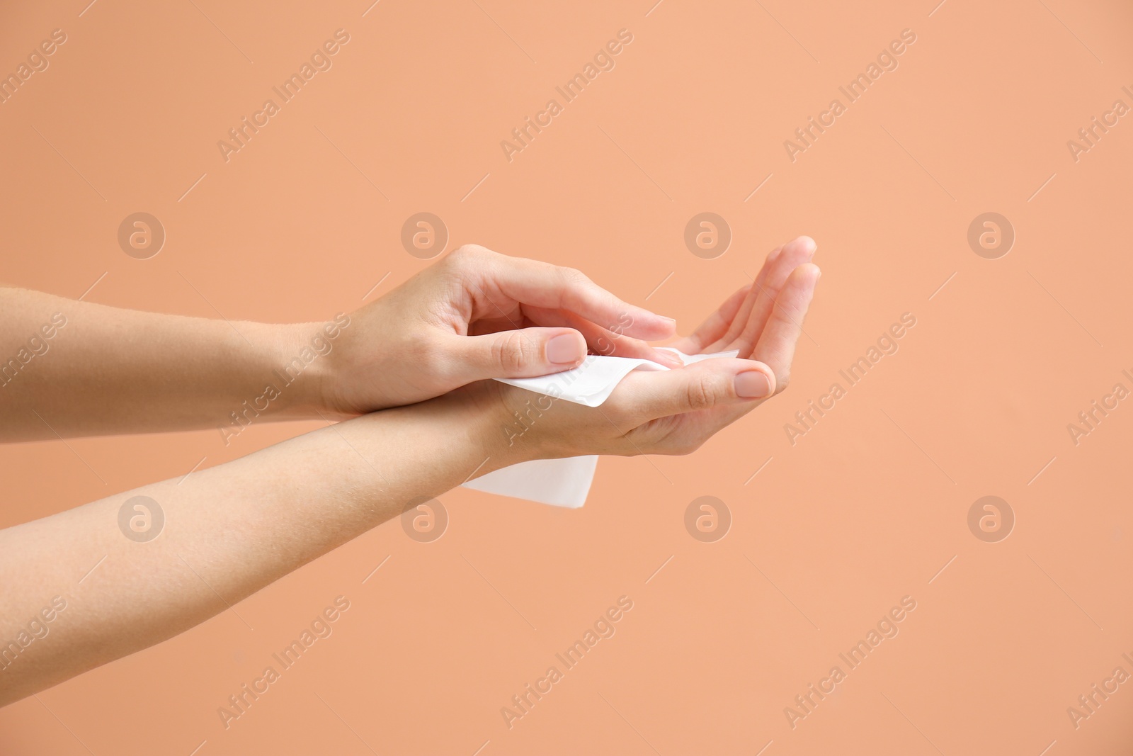 Photo of Woman cleaning hands with paper tissue on light brown background, closeup