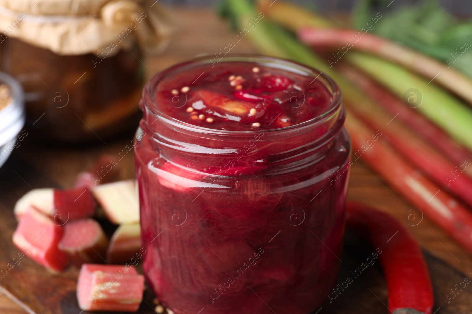 Photo of Tasty rhubarb sauce in glass jar on table, closeup view