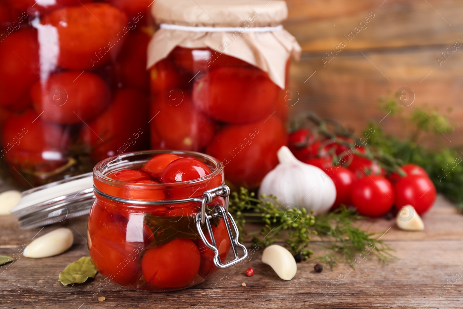 Photo of Glass jar of pickled cherry tomatoes on wooden table. Space for text