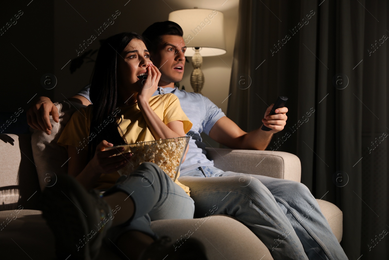 Photo of Couple watching movie with popcorn on sofa at night