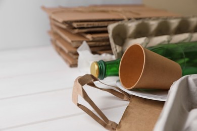 Photo of Heap of waste paper and glass bottle on white wooden table, closeup. Space for text