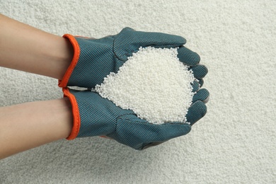 Photo of Woman holding pile of granular mineral fertilizer over grains, top view