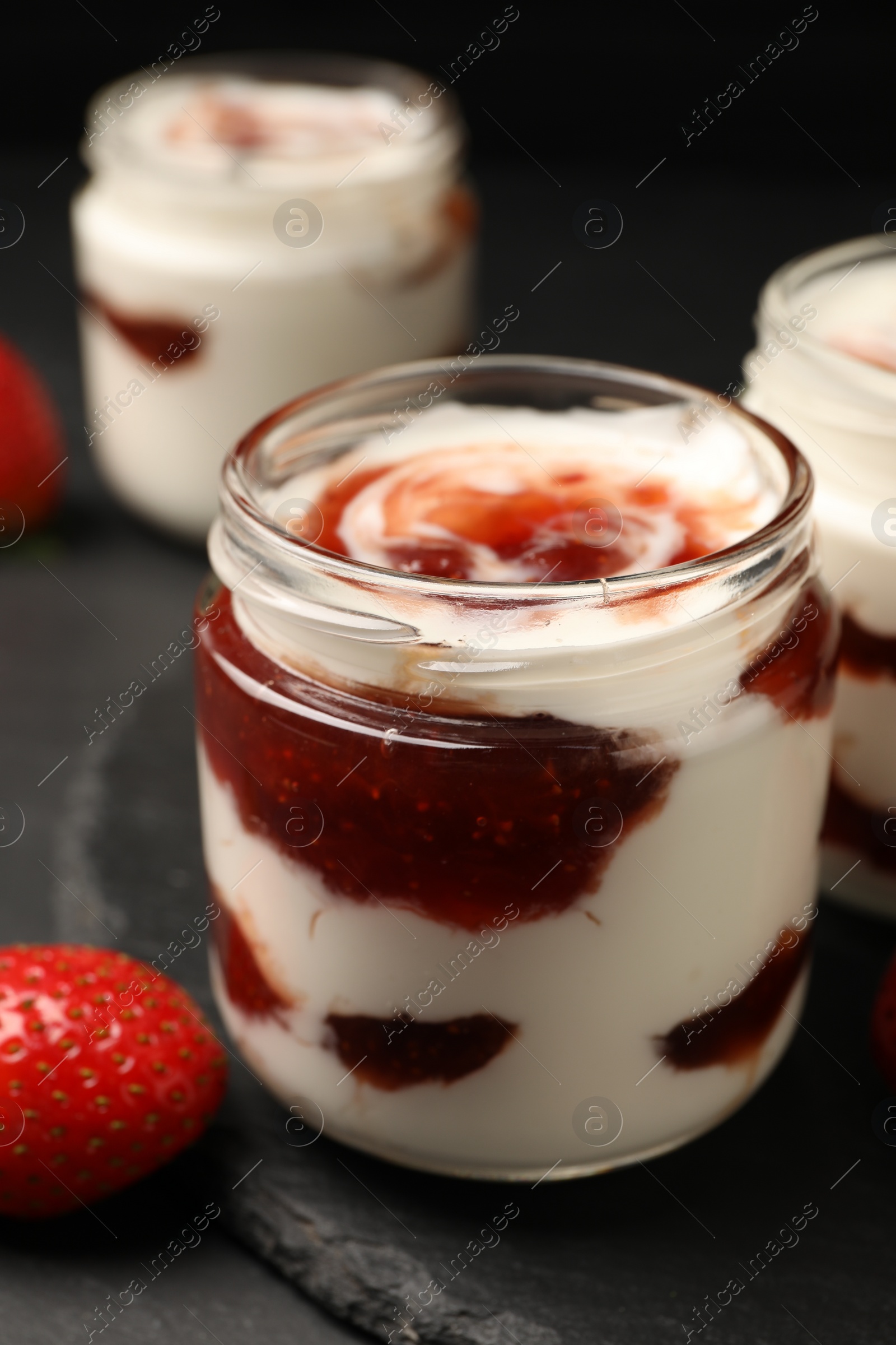 Photo of Tasty yoghurt with jam and strawberry on black table, closeup