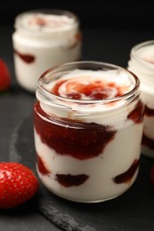 Photo of Tasty yoghurt with jam and strawberry on black table, closeup