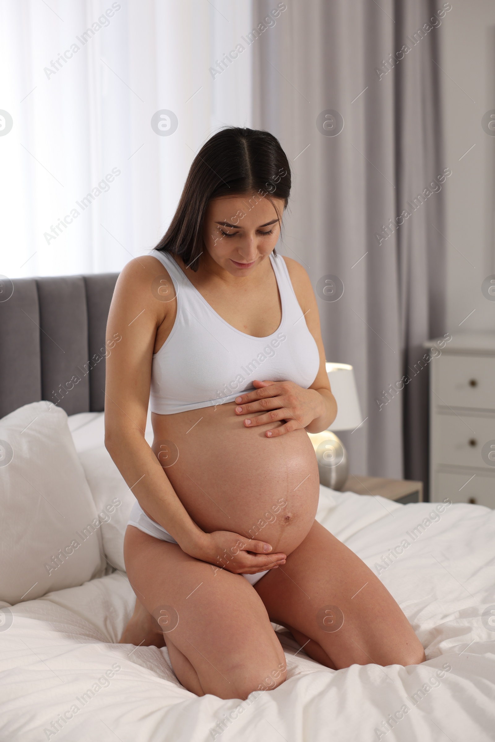 Photo of Beautiful pregnant woman in stylish comfortable underwear on bed at home