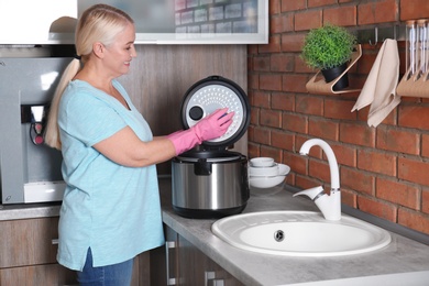 Mature woman cleaning modern multi cooker at kitchen counter