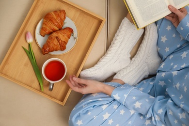 Photo of Woman with cup of tea and book resting on sofa, top view