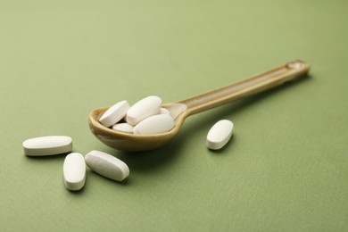 Vitamin pills in spoon on olive background, closeup