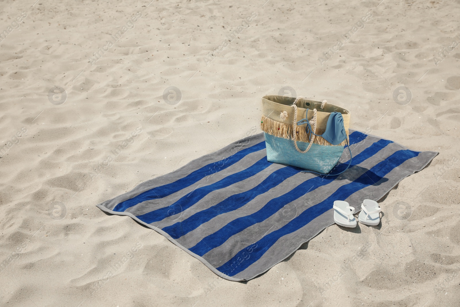 Photo of Beach towel with bag, flip flops and swimsuit on sand