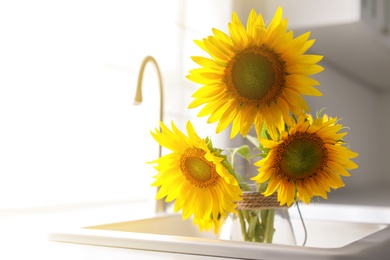 Photo of Vase with beautiful yellow sunflowers in kitchen sink, space for text