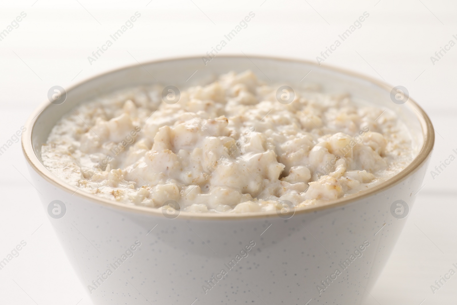 Photo of Tasty boiled oatmeal in bowl on white table, closeup