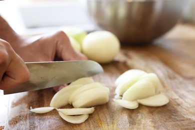 Photo of Woman cutting fresh ripe onion on wooden board, closeup. Space for text