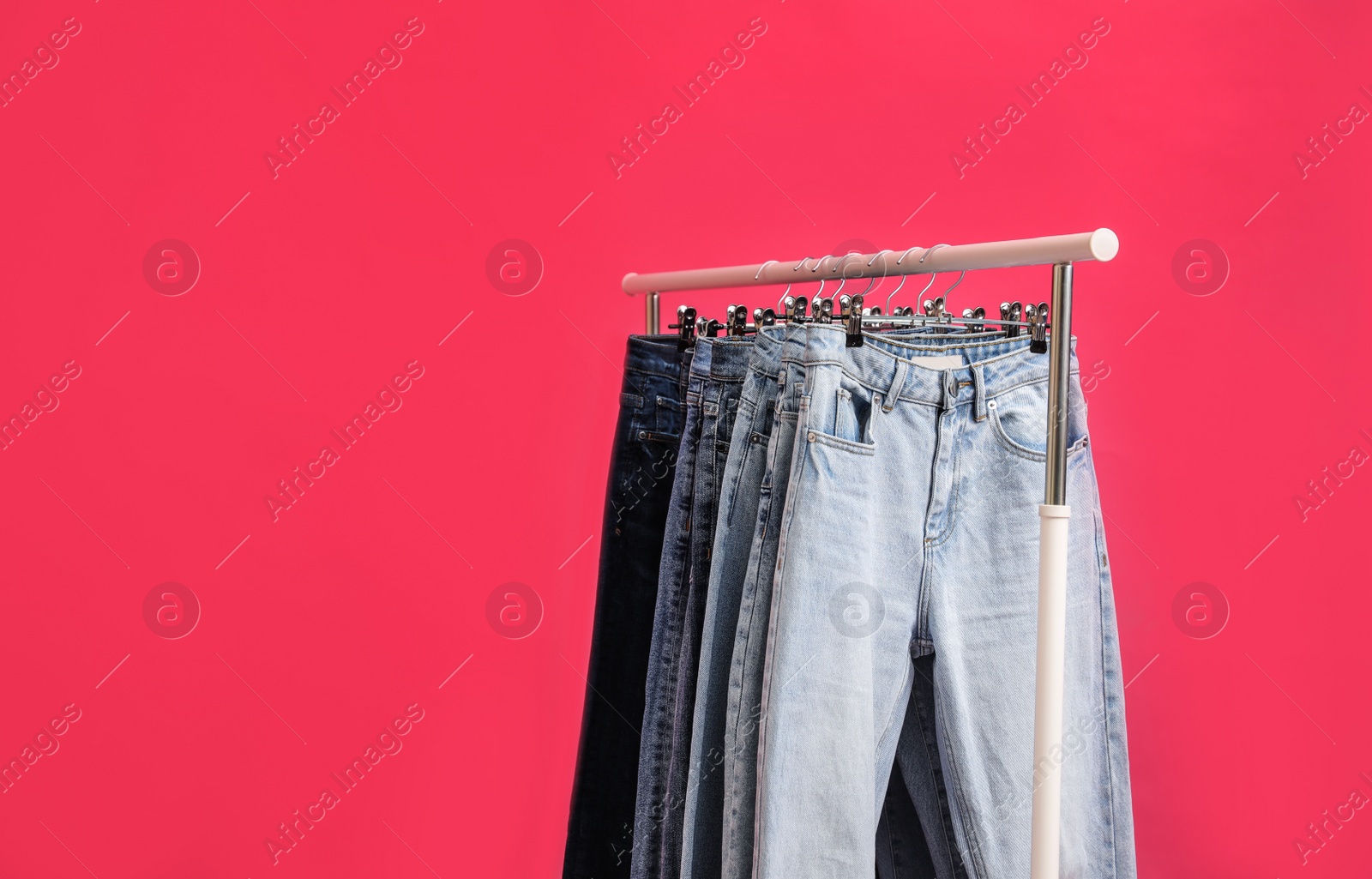Photo of Rack with stylish jeans on pink background, closeup. Space for text