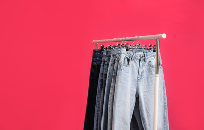 Photo of Rack with stylish jeans on pink background, closeup. Space for text