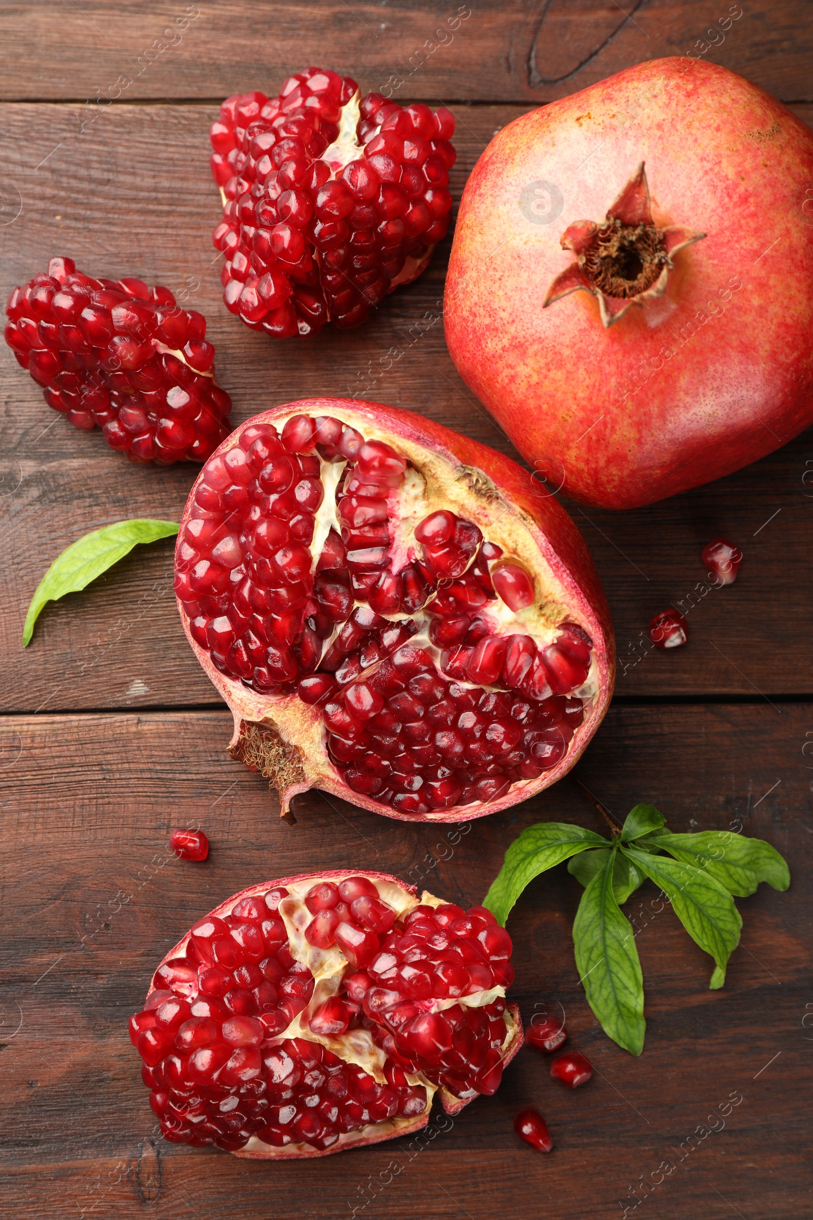 Photo of Fresh pomegranates and green leaves on wooden table, flat lay