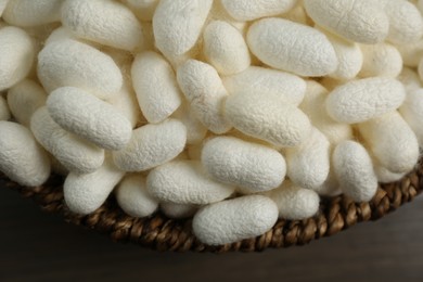 Photo of White silk cocoons in bowl on wooden table, closeup