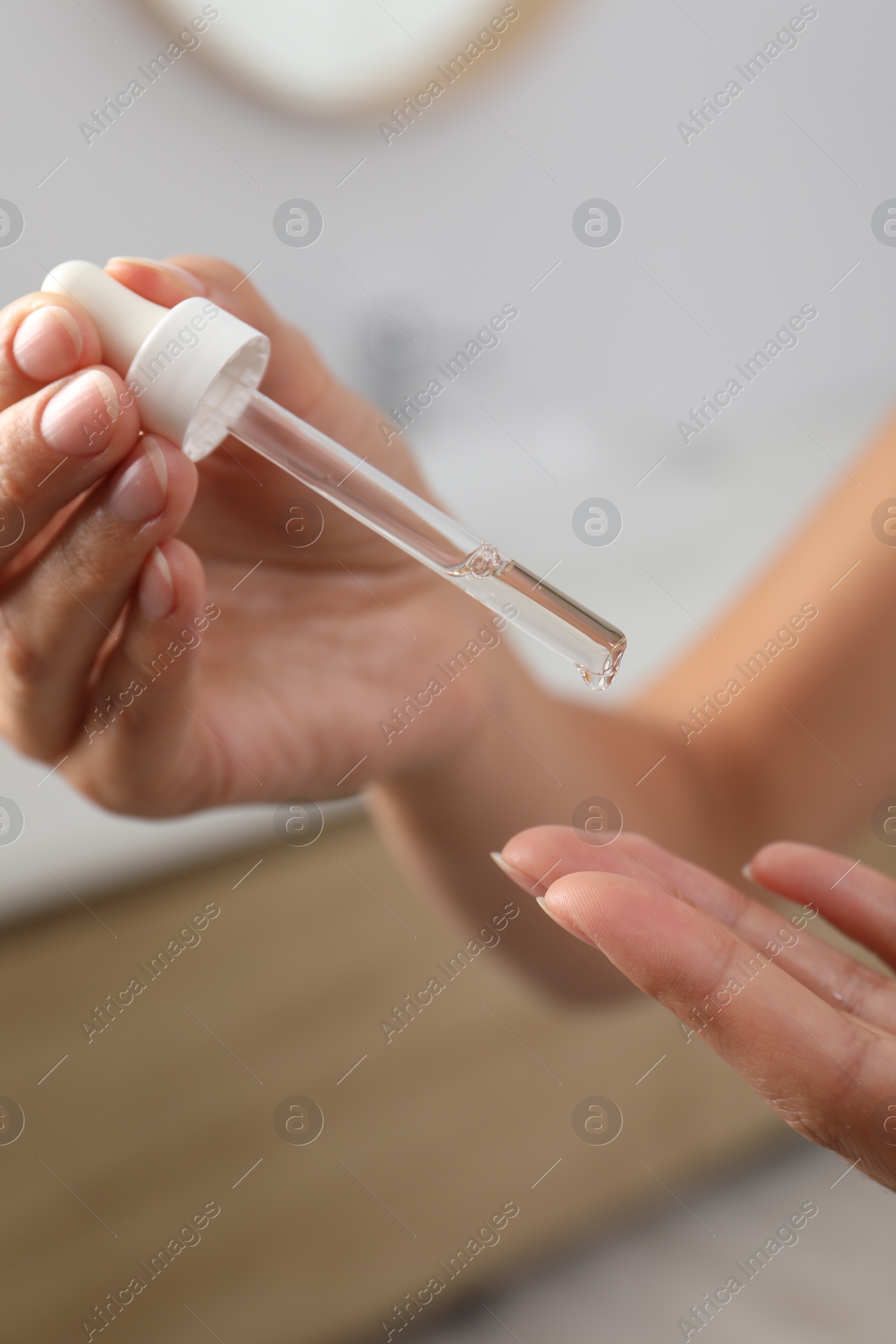 Photo of Woman applying cosmetic serum onto her finger on blurred background, closeup