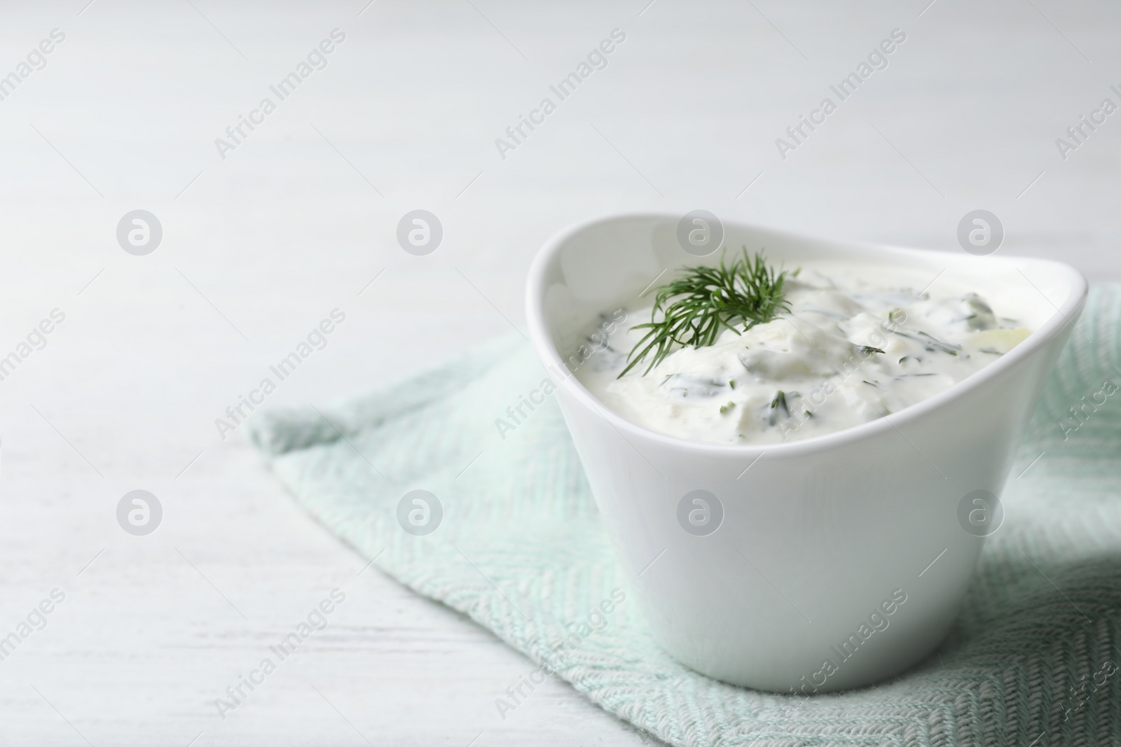 Photo of Cucumber sauce in ceramic bowl on wooden background, space for text. Traditional Tzatziki