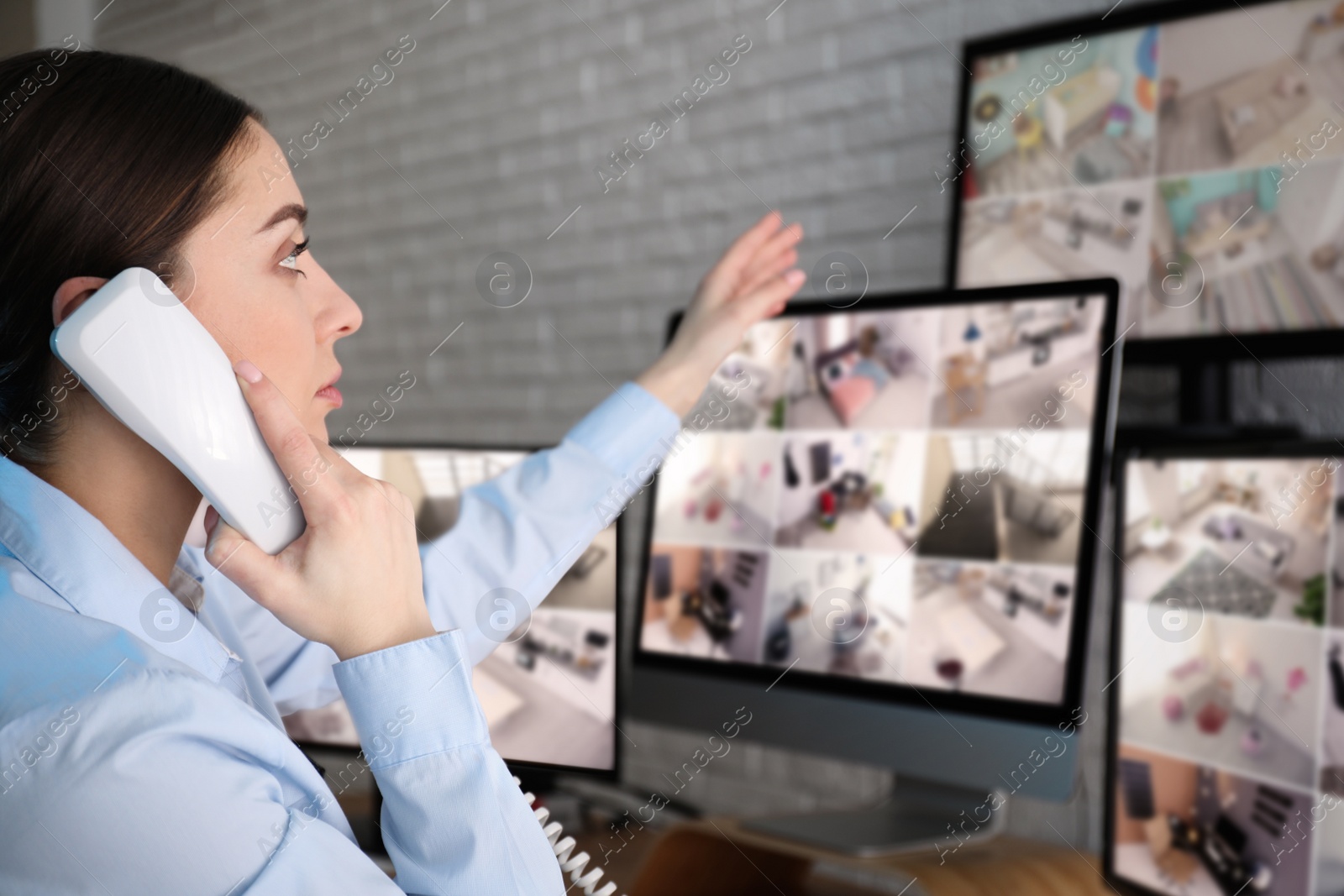 Photo of Female security guard talking by telephone near monitors at workplace