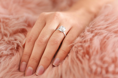 Young woman wearing beautiful engagement ring on faux fur rug, closeup
