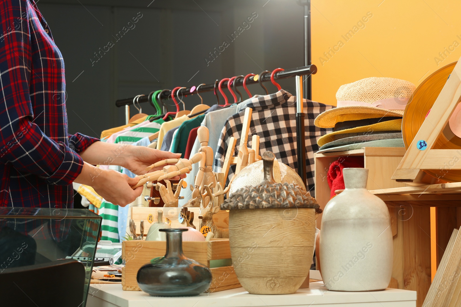 Photo of Woman holding wooden figure near table with different stuff indoors, closeup. Garage sale