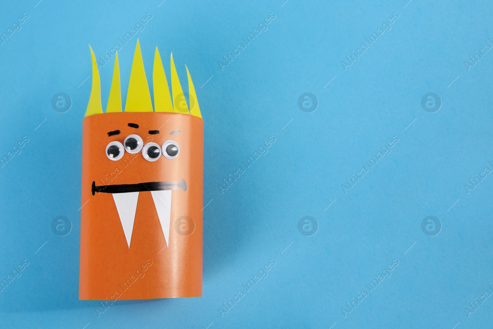 Photo of Funny orange monster on light blue background, top view with space for text. Halloween decoration