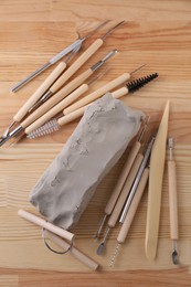 Clay and set of modeling tools on wooden table, flat lay