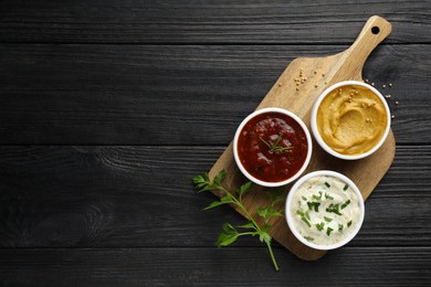 Different tasty sauces in bowls and parsley on black wooden table, top view. Space for text