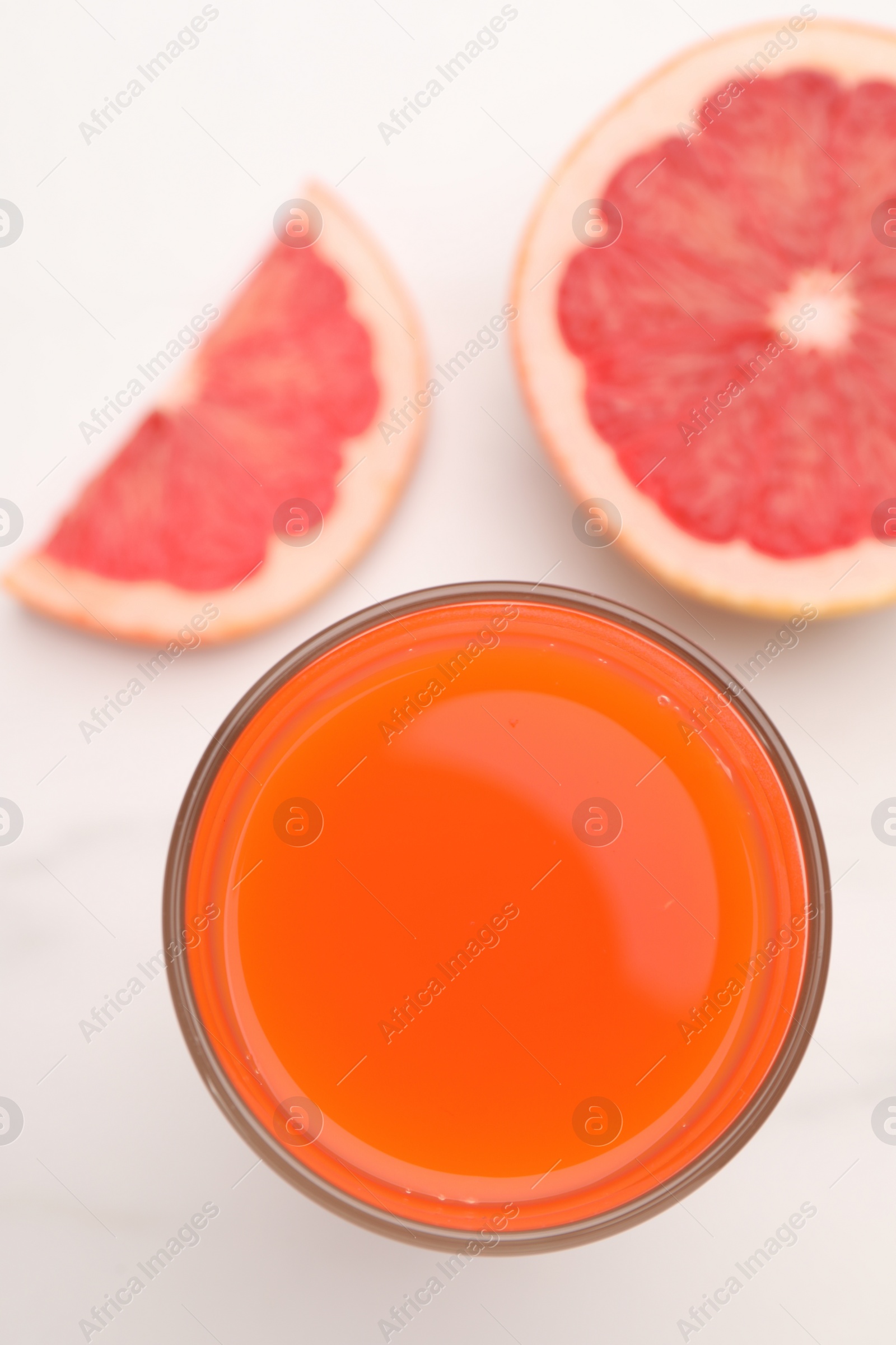 Photo of Tasty grapefruit juice in glass and slices of fresh fruit on white table, top view