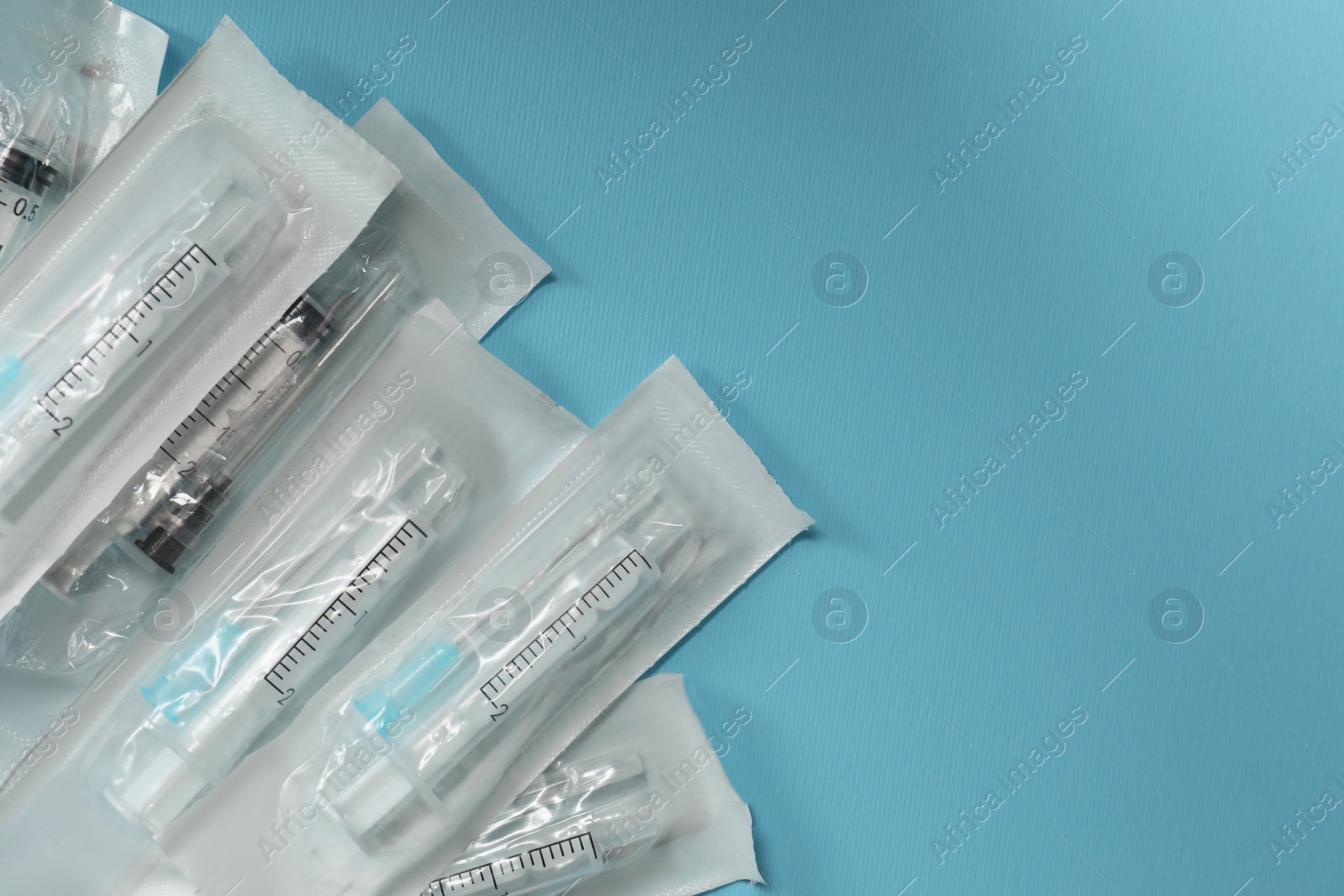 Photo of Packed disposable syringes with needles on light blue background, flat lay. Space for text