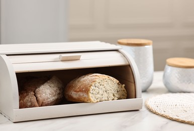 Wooden bread basket with freshly baked loaves on white marble table in kitchen