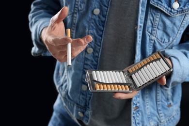 Photo of Man taking cigarette from case on black background, closeup