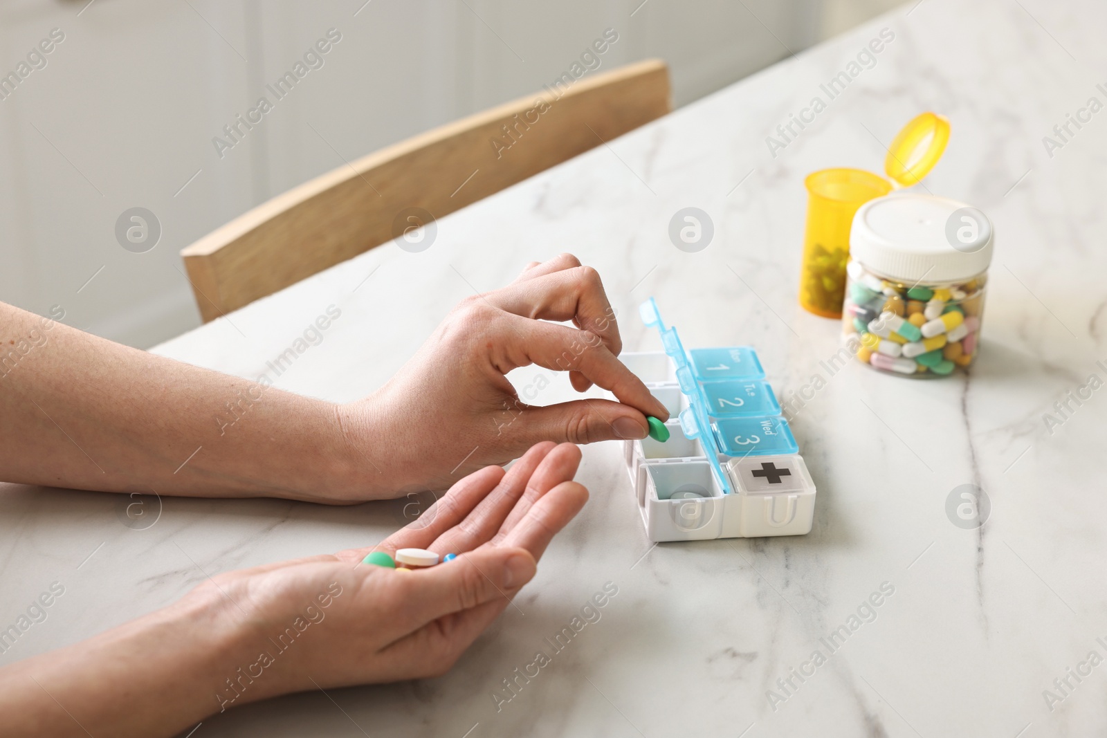 Photo of Woman with pills and organizer at white marble table, closeup