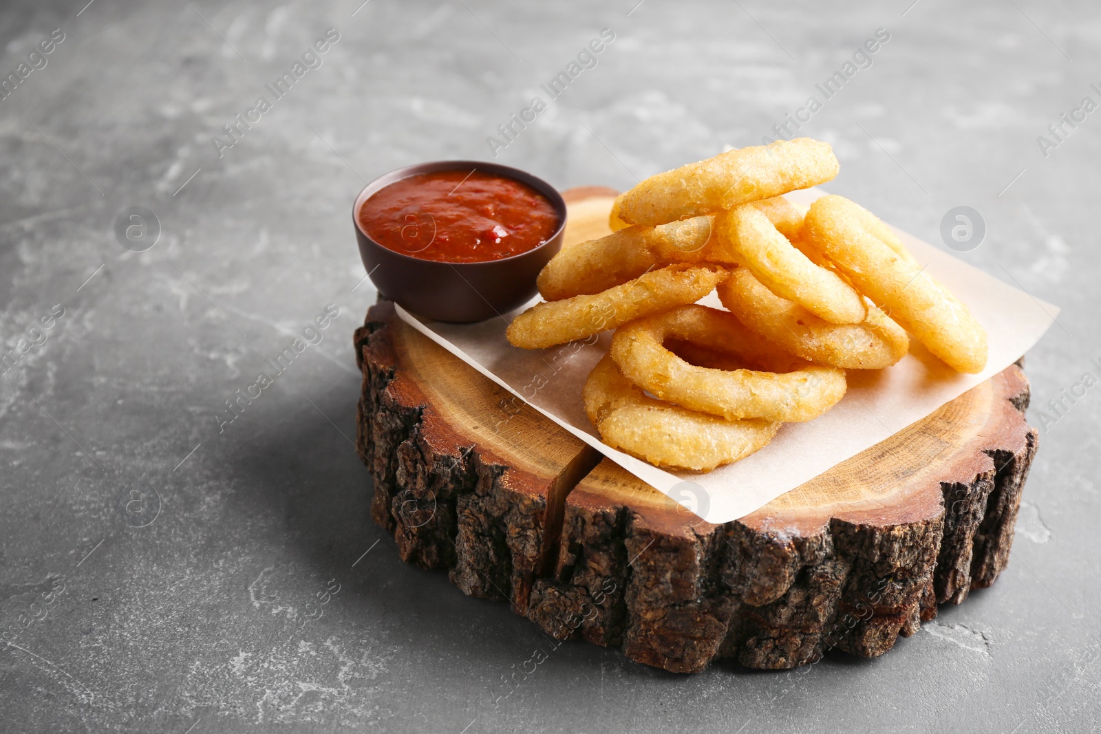 Photo of Tasty onion rings and bowl of sauce on gray table