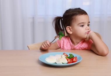 Photo of Cute little girl refusing to eat her breakfast at home, space for text