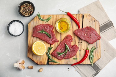 Photo of Fresh raw meat steaks and spices on light grey table, flat lay