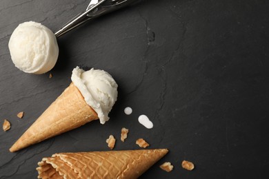 Photo of Ice cream scoops in wafer cones on dark gray textured table, flat lay. Space for text
