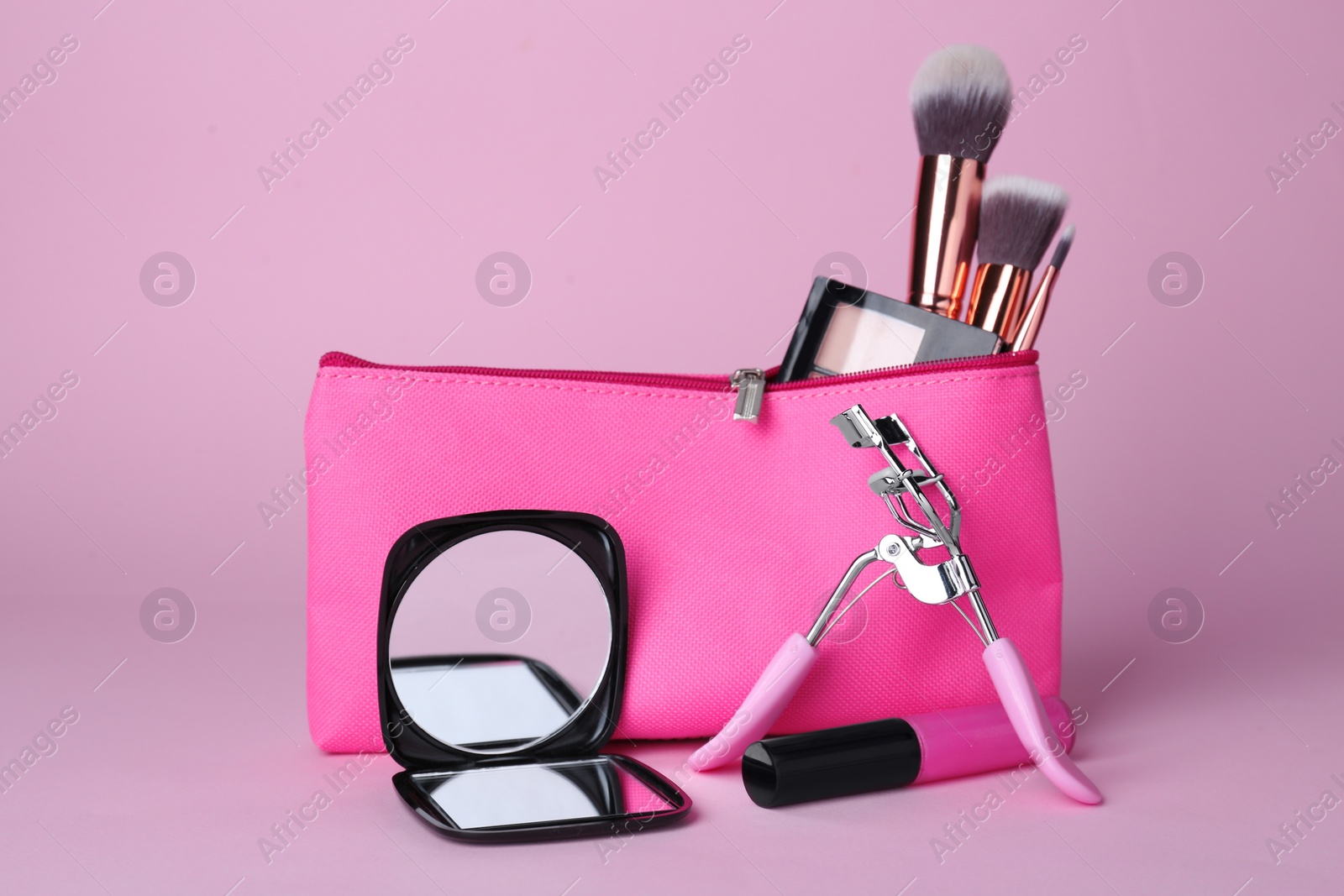 Photo of Stylish pocket mirror and cosmetic bag with makeup products on violet background