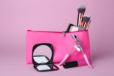 Stylish pocket mirror and cosmetic bag with makeup products on violet background