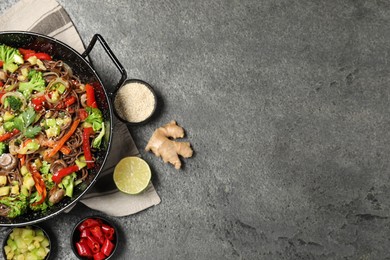 Photo of Wok with noodles, mushrooms, vegetables and other products on grey table, flat lay. Space for text