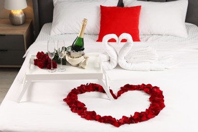 Photo of Honeymoon. Swans made with towels, heart of beautiful rose petals and sparkling wine on bed in room