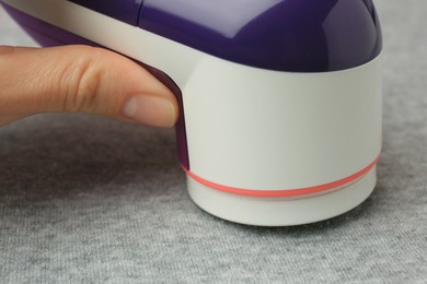 Woman using fabric shaver on light grey cloth with lint, closeup