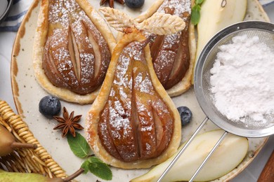 Delicious pears baked in puff pastry with powdered sugar served on table, top view